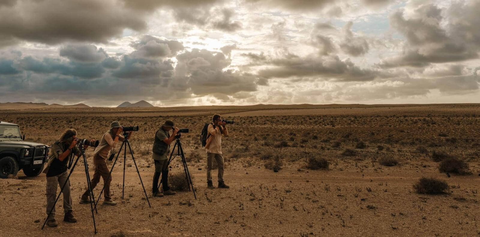 Vier Personen mit Teleobjektiven und Stativen fotografieren Vögel in einer kargen Landschaft.