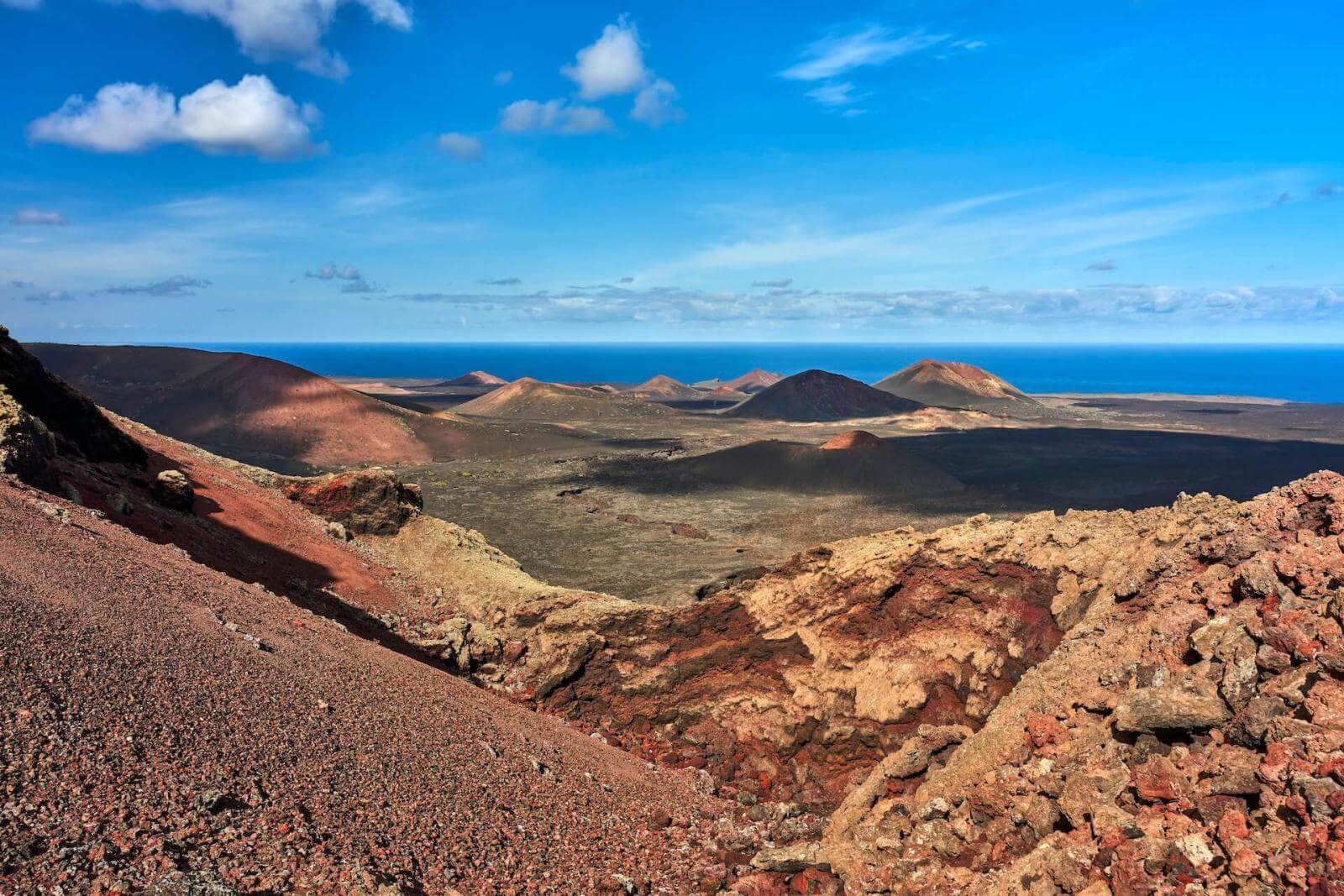 Vulkanlandschaft im Nationalpark Timanfaya, Lanzarote, mit Lavaströmen, Bergen und Meer im Hintergrund.
