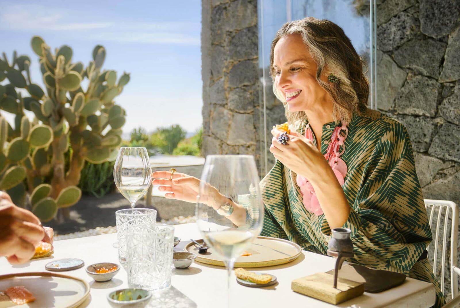 Eine Person sitzt an einem Tisch neben der Terrassentür mit Kakteen im Hintergrund und genießt einen Aperitif und ein Glas Wein.