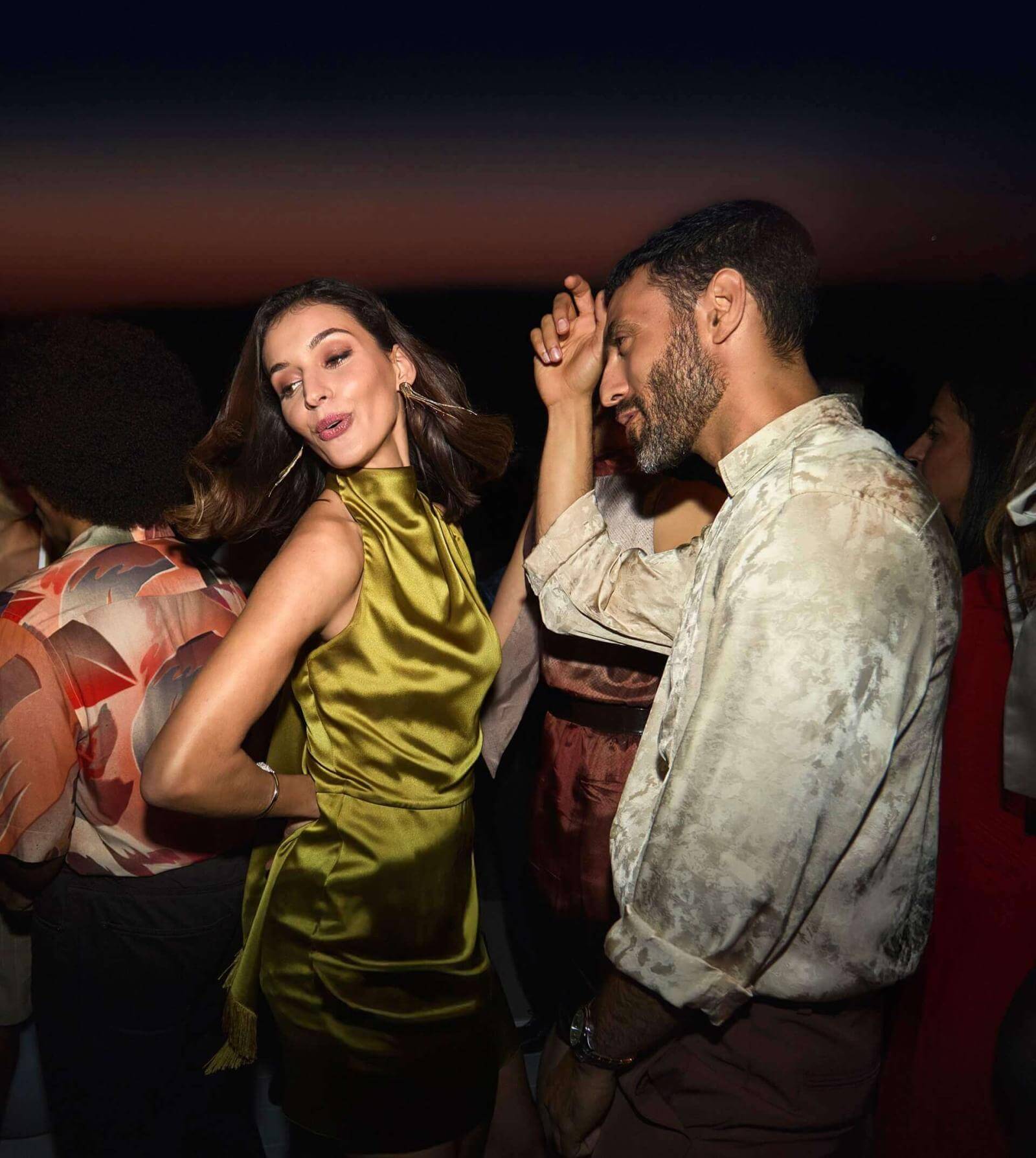 Ein Paar tanzt nach Sonnenuntergang auf einer Rooftop-Terrasse mit Blick aufs Meer.