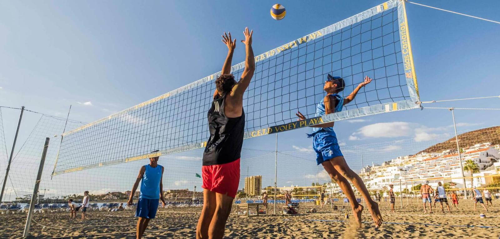 Menschen spielen Beachvolleyball und springen hoch, um einen Ball zu erreichen.