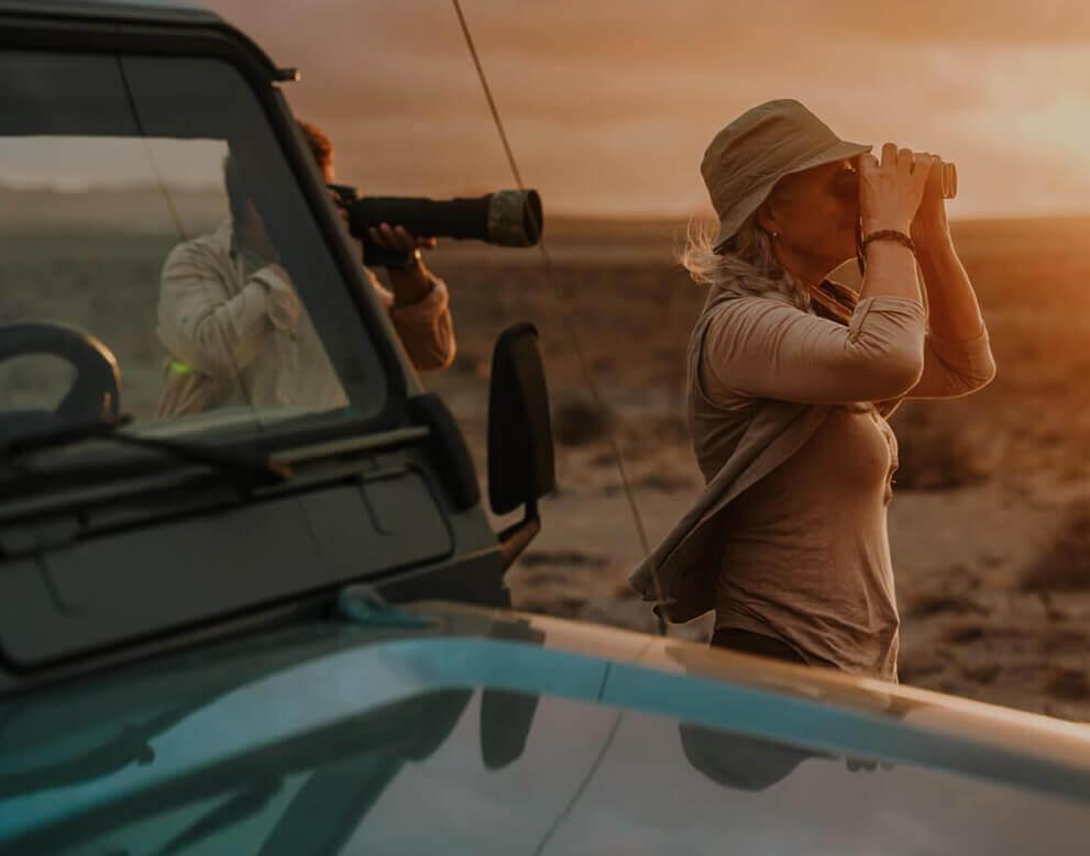 Eine Person mit Fernglas beobachtet Vögel bei Sonnenuntergang neben einem Geländewagen.