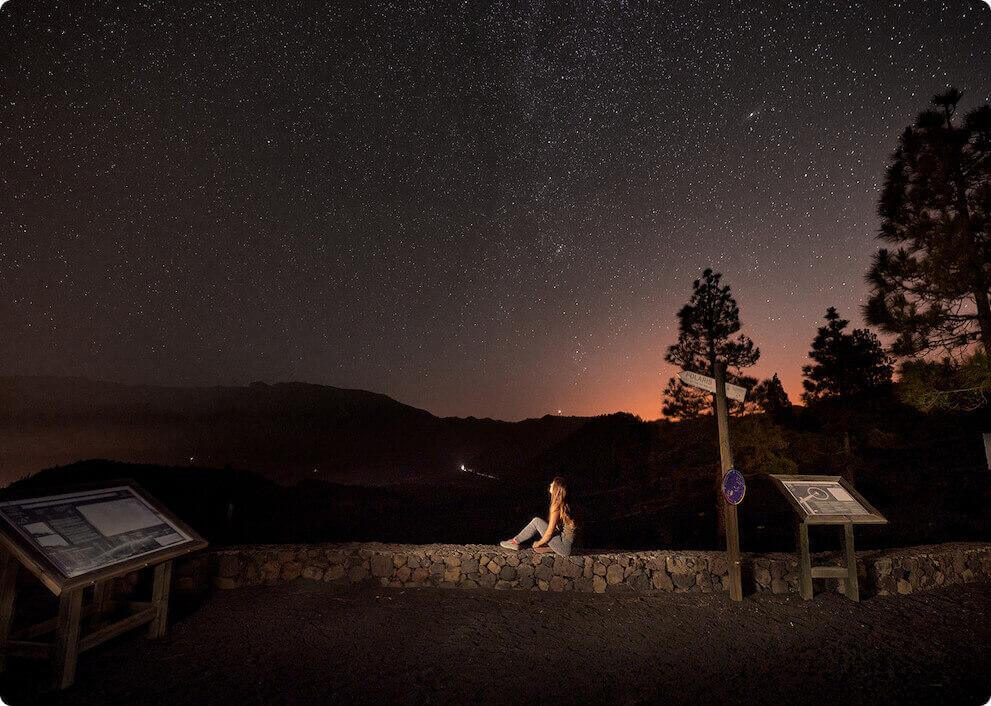 Sternenhimmel am Aussichtspunkt Llano del Jable, La Palma, mit Bergsilhouetten und einem staunenden Menschen.