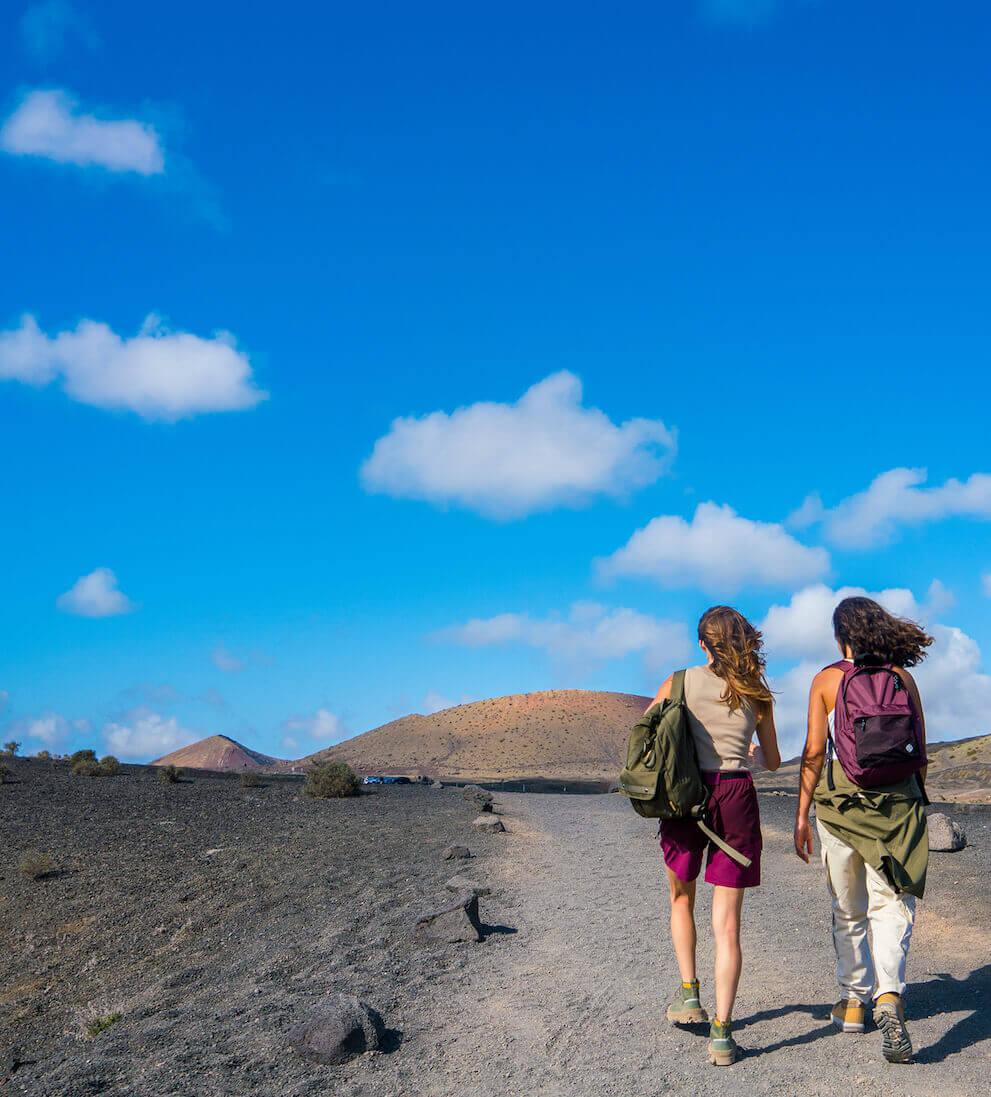 Zwei Personen unter blauem Himmel, die auf einem Vulkanpfad im Nationalpark Timanfaya wandern.