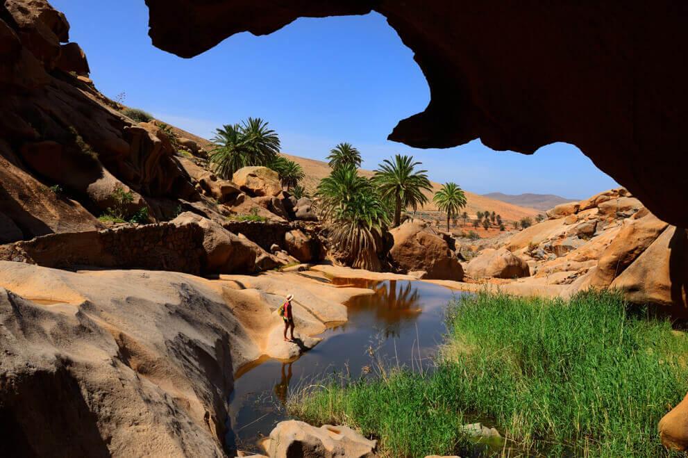 Die Schlucht Las Peñitas auf Fuerteventura mit Felsen, Palmen und kleinem Pool inmitten karger Landschaft.