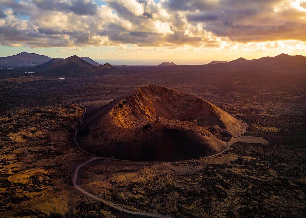 Luftaufnahme des Vulkans Cuervo auf Lanzarote, dessen Krater im Licht der untergehenden Sonne leuchtet.